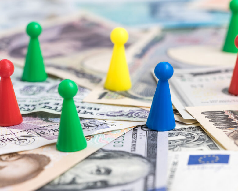 World money game by colorful plastic game figurines on international major countries banknotes, US dollar, Japanese yen, Euro, Chinese yuan.