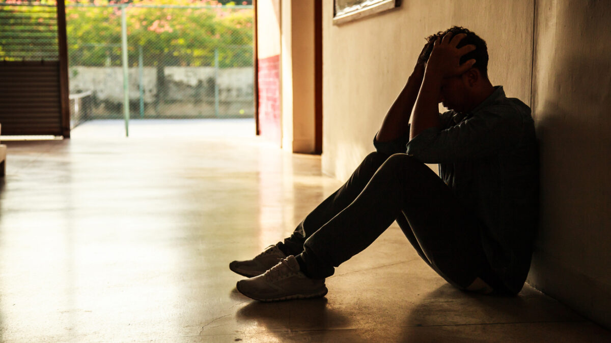 Emotional moment: man sitting holding head in hands, stressed sad young male having mental problems, feeling bad, depressed, disappointed, hopeless. Desperate man in the dark corner needing help.