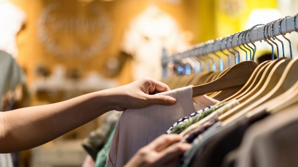 Close up of woman hand choosing thrift young and discount t-shirt clothes in store, searching or buying cheap cotton shirt on rack hanger at flea market , stall shopping apparel fashion concept