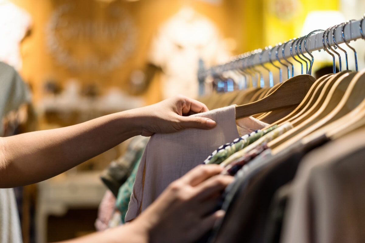 Close up of woman hand choosing thrift young and discount t-shirt clothes in store, searching or buying cheap cotton shirt on rack hanger at flea market , stall shopping apparel fashion concept