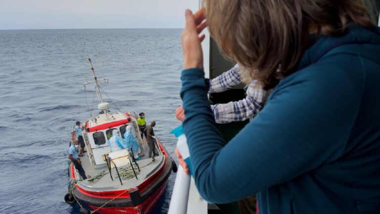 Επιβάτες του κρουαζιερόπλοιου MV Hondius, παρακολουθούν επιδημιολόγους να επιβιβάζονται στο πλοίο στην Πράια, κατά τη διάρκεια του ταξιδιού τους προς το ισπανικό λιμάνι της Τενερίφης, στις 6 Μαΐου 2026 AP Photo