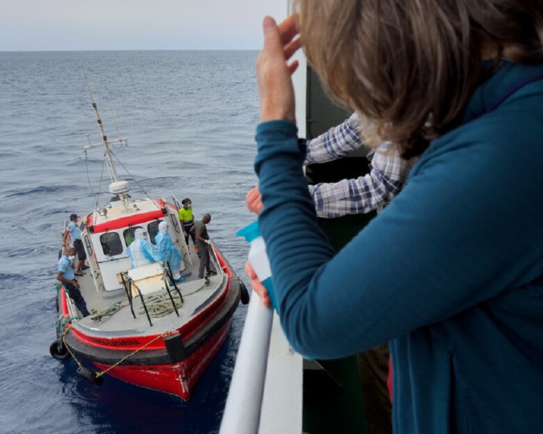 Επιβάτες του κρουαζιερόπλοιου MV Hondius, παρακολουθούν επιδημιολόγους να επιβιβάζονται στο πλοίο στην Πράια, κατά τη διάρκεια του ταξιδιού τους προς το ισπανικό λιμάνι της Τενερίφης, στις 6 Μαΐου 2026 AP Photo
