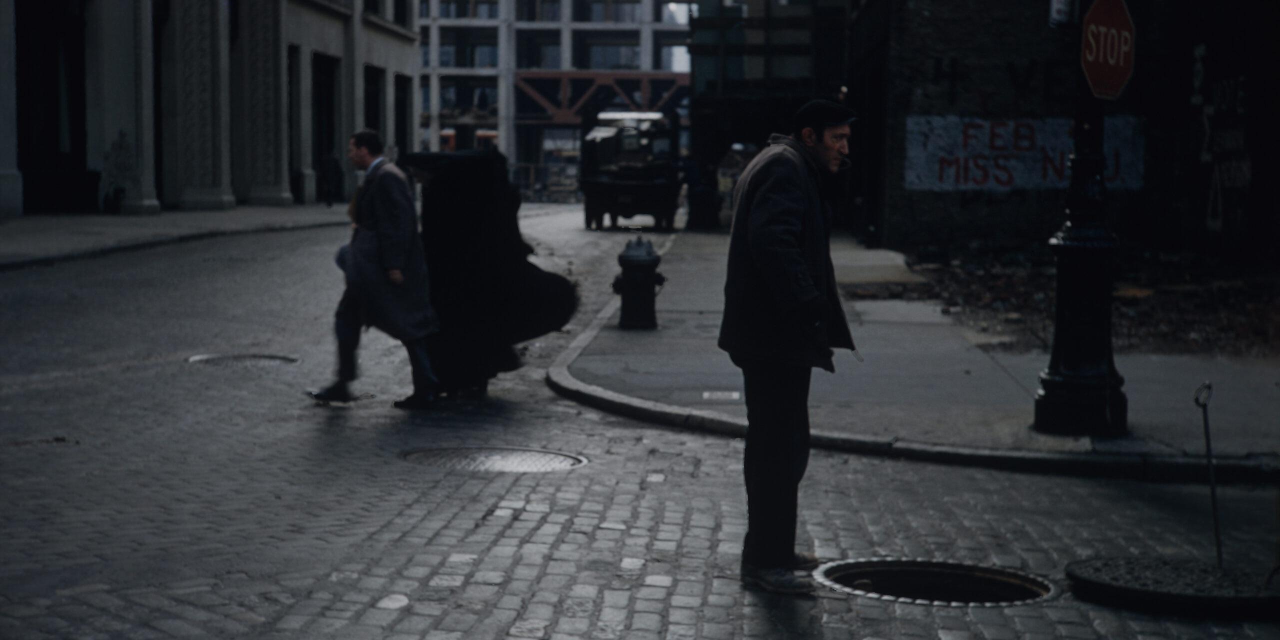 A man in a cap stand at the edge of an open manhole on a brick-lined street in Tribeca, New York
