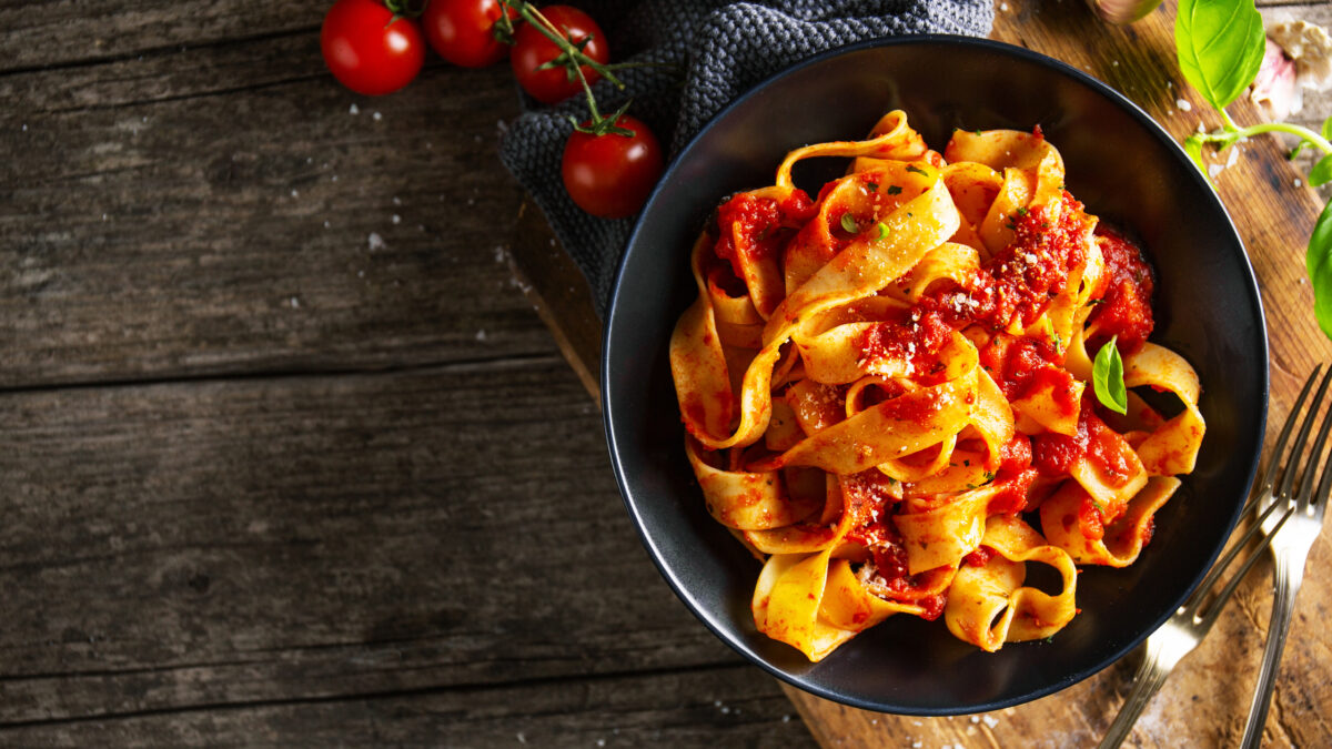 Tasty appetizing pasta tagliatelle spaghetti with tomato sauce and parmesan. Served on plate on wooden table. Closeup. Horizontal with copy space.