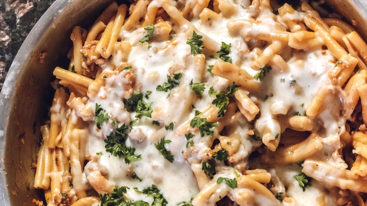 Close up of pasta casserole baked in a skillet topped with melted cheese and fresh parsley