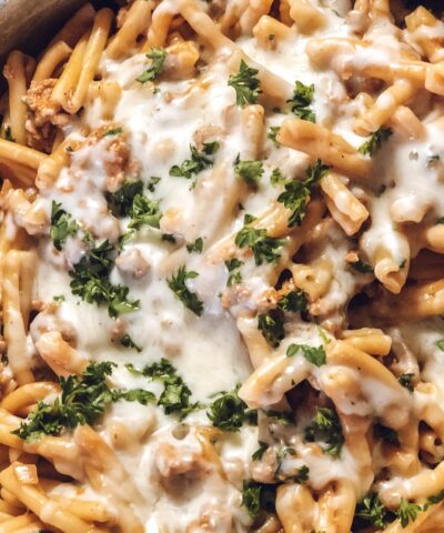Close up of pasta casserole baked in a skillet topped with melted cheese and fresh parsley