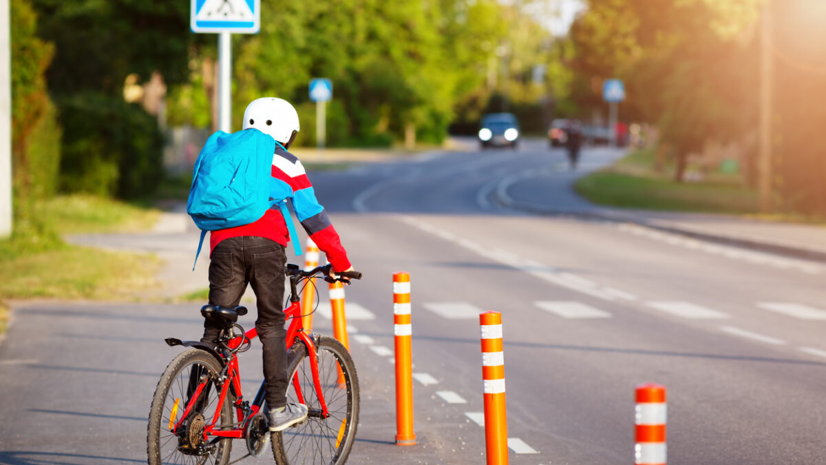 Child with rucksack riding on bikes in the park near school. Pupil with backpack outdoors.