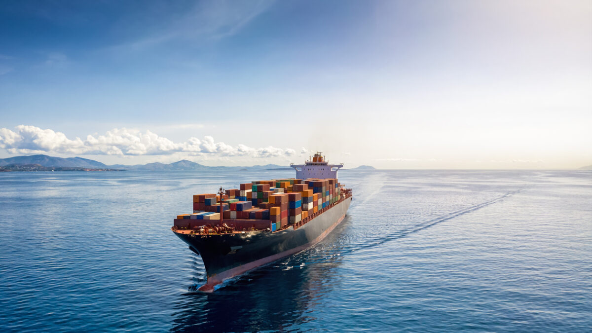 Aerial view of a heavy loaded container cargo vessel traveling over calm, blue sea