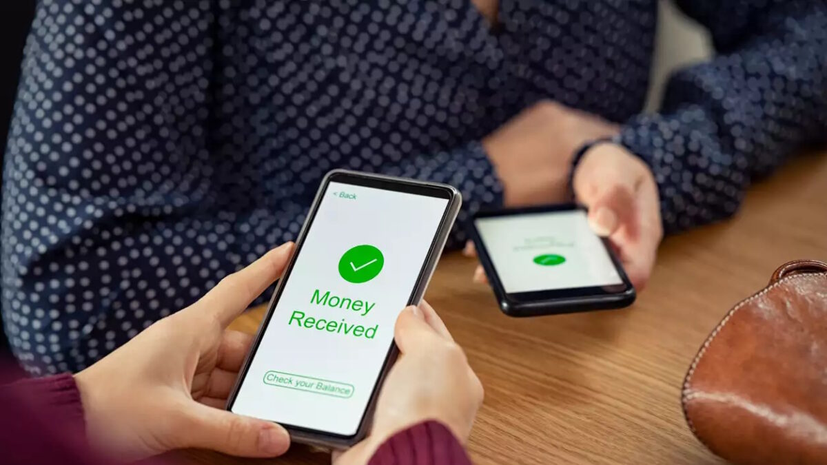 Close up of woman hands holding mobile phone with application to receive money. People holding smart phone and making cashless payment transaction in a shop. Close up of smartphone screen displaying payment sent with money received message.