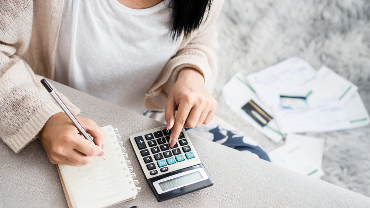 woman writing a list of debt on notebook calculating her expenses with calculator with many invoices , female hand doing accounting