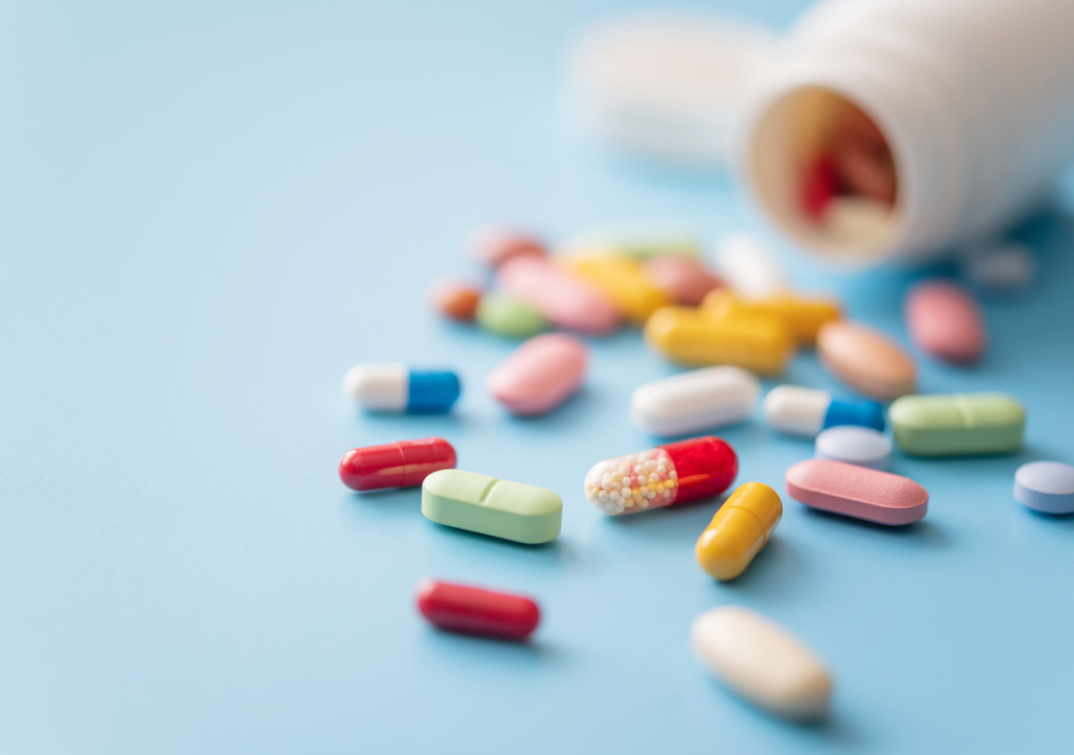 Colorful Pills scattered from white plastic medicine container on blue background.
