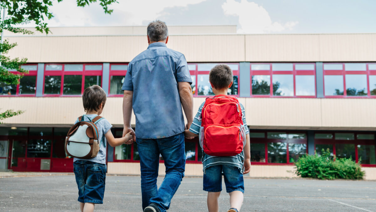 Back to school. View from the back of a happy dad escorts his sons schoolchildren to school. Parental care for children.