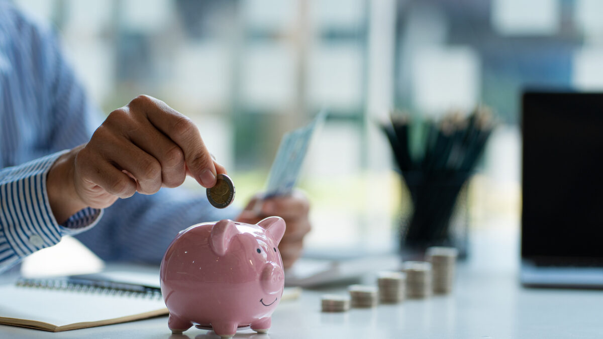 Hands of a young Asian businessman Man putting coins into piggy bank and holding money side by side to save expenses A savings plan that provides enough of his income for payments.
