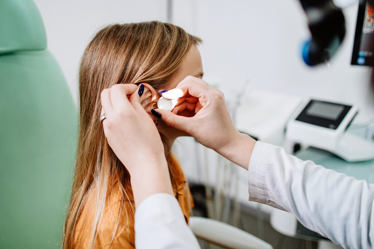Female audiologist examining girl ear using otoscope in doctors office. Child receiving a ear exam. Nose and throat medical examination. Healthcare and medicine concept.
