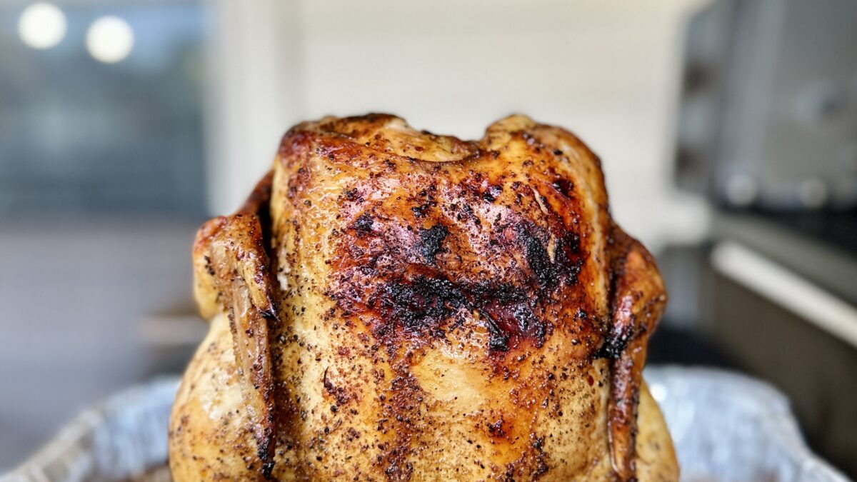 A beer can chicken, seasoned with spices and flavored by the beer inside of the can, is perched on a beer can chicken stand shortly after coming off a backyard barbecue grill.