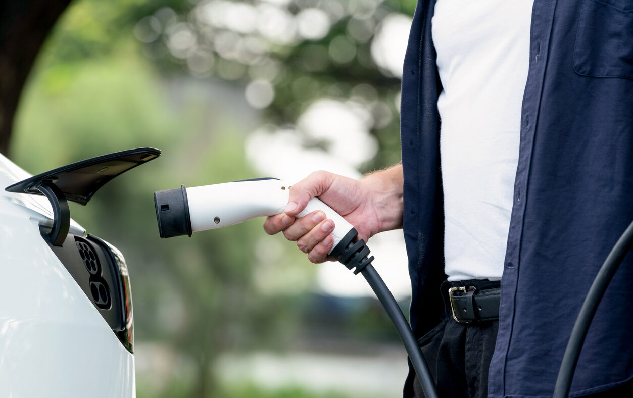 Man recharging battery for electric car during road trip travel EV car in natural forest or national park. Eco friendly travel during vacation and holiday. Exalt