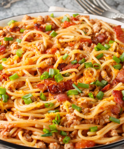 Delicious spaghetti with bacon, minced meat, cheddar cheese, onion and spicy tomato sauce close-up in a plate on the table. Horizontal