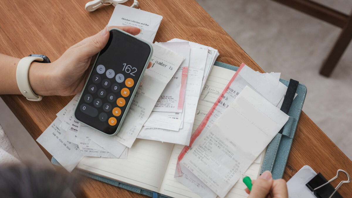 Close up a woman managing her home finances with a smartphone, she reviews financial bills. Concepts include financial planning, taxes, spending, budgeting, and financial challenges.