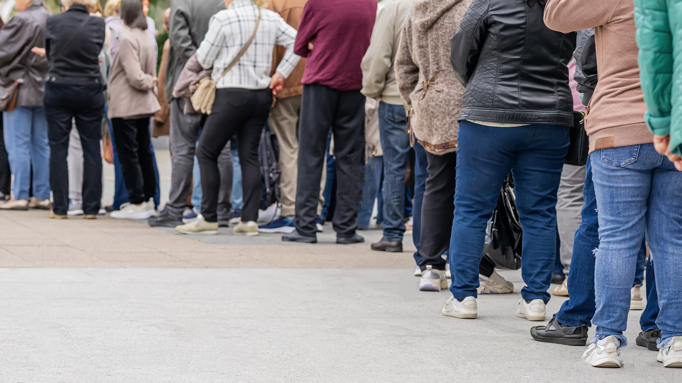 Group of anonymous diverse people standing in queue outdoors, long line of men and women, rear view. Concept of waiting, patience and urban life