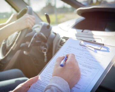 Examiner filling in driver's license road test form sitting with her student inside a car