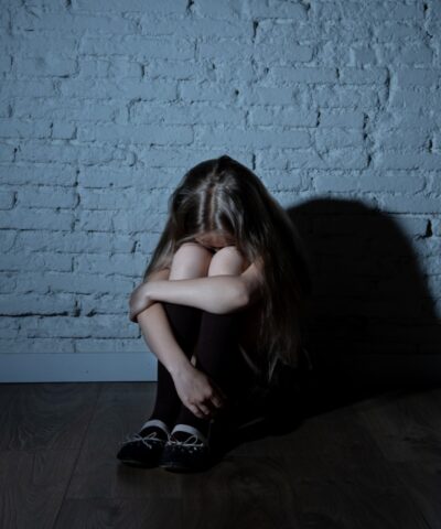 Sad desperate young girl suffering from bulling and harassment felling lonely, unhappy desperate and hopeless sitting against the wall, dark light. School isolation, abuse and bullying concept