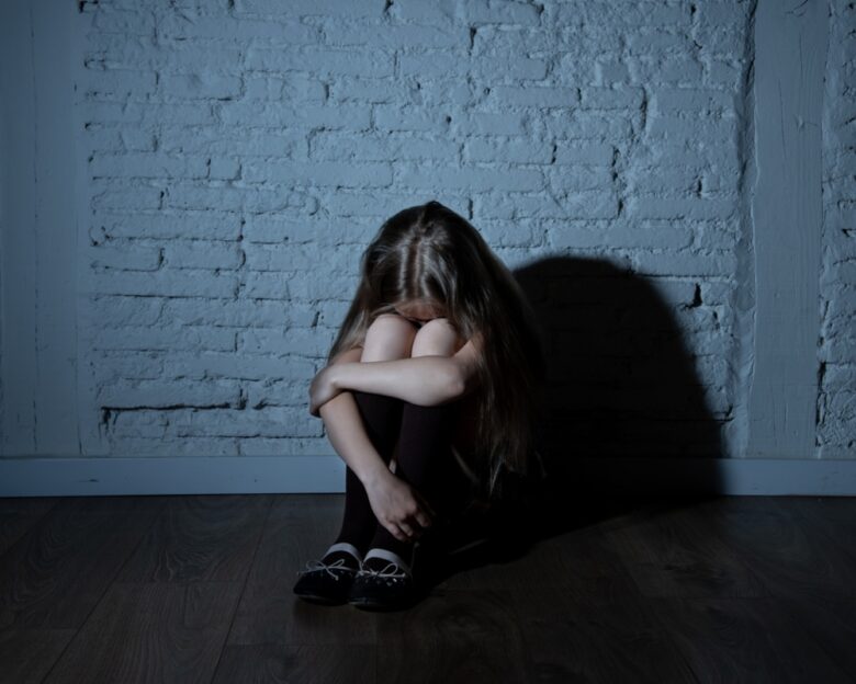Sad desperate young girl suffering from bulling and harassment felling lonely, unhappy desperate and hopeless sitting against the wall, dark light. School isolation, abuse and bullying concept