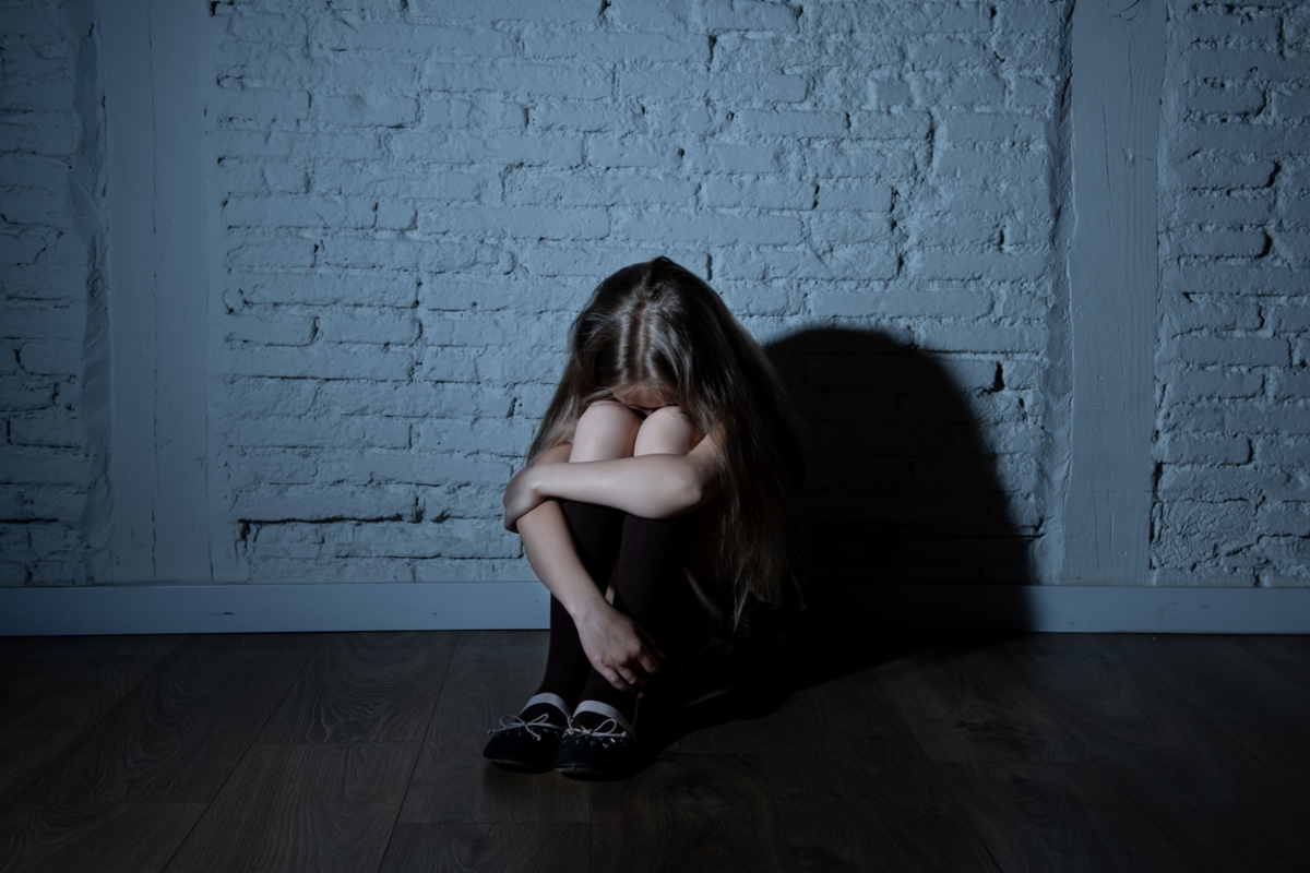 Sad desperate young girl suffering from bulling and harassment felling lonely, unhappy desperate and hopeless sitting against the wall, dark light. School isolation, abuse and bullying concept