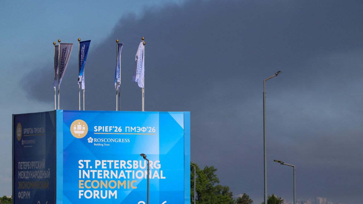 Police officers stand in front of a banner and flags witah the logo of the St. Petersburg International Economic Forum (SPIEF) as heavy smoke billows in the background after drones hit infrastructure, according to the governor Alexander Beglov, in St Petersburg, Russia June 3, 2026. REUTERS/Stringer