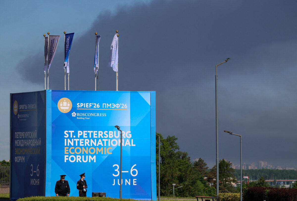 Police officers stand in front of a banner and flags witah the logo of the St. Petersburg International Economic Forum (SPIEF) as heavy smoke billows in the background after drones hit infrastructure, according to the governor Alexander Beglov, in St Petersburg, Russia June 3, 2026. REUTERS/Stringer