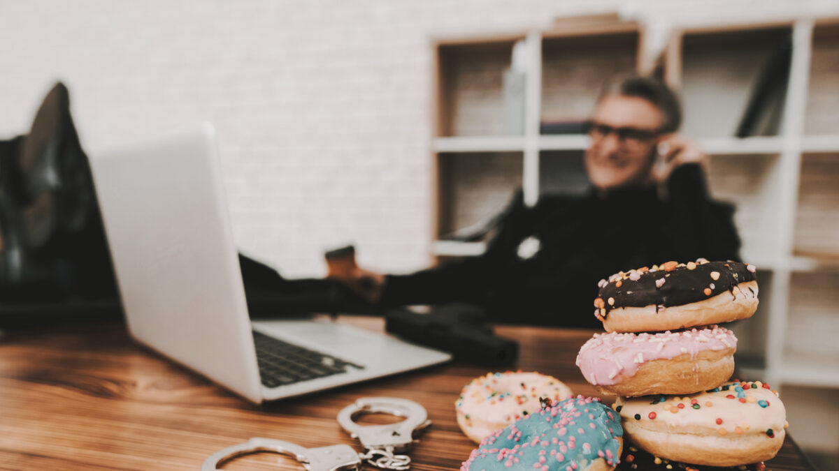Smiling Policeman In Department Office. Relaxing Concept. Coffee Break. Cop's Donuts. Working Together. Citizen's Protection. Public Order. Phone Talking. Handscuffs On Table. Detective Uniform.
