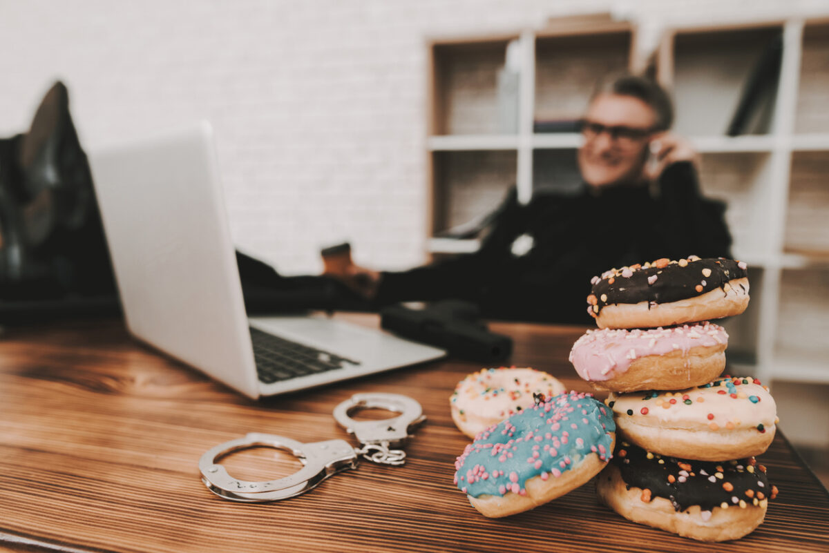 Smiling Policeman In Department Office. Relaxing Concept. Coffee Break. Cop's Donuts. Working Together. Citizen's Protection. Public Order. Phone Talking. Handscuffs On Table. Detective Uniform.