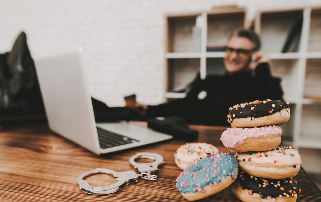 Smiling Policeman In Department Office. Relaxing Concept. Coffee Break. Cop's Donuts. Working Together. Citizen's Protection. Public Order. Phone Talking. Handscuffs On Table. Detective Uniform.