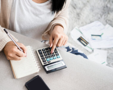 woman writing a list of debt on notebook calculating her expenses with calculator with many invoices , female hand doing accounting