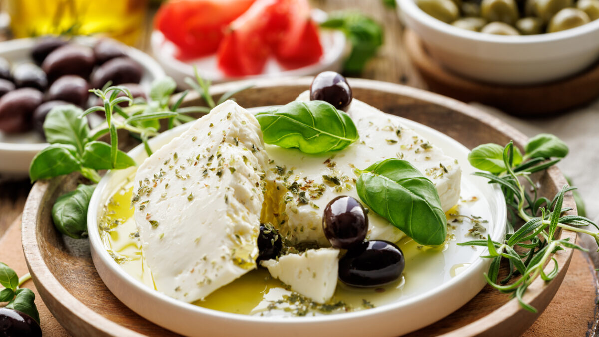Feta cheese with the addition of olive oil, olives and herbs on a ceramic plate on a rustic wooden table. Traditional Greek products