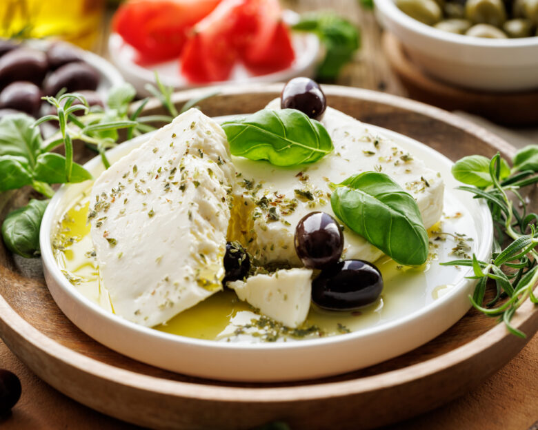 Feta cheese with the addition of olive oil, olives and herbs on a ceramic plate on a rustic wooden table. Traditional Greek products