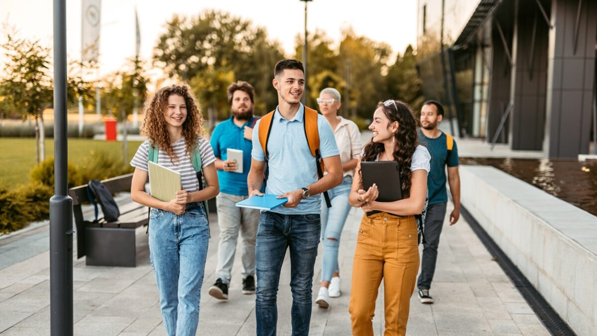 Group of friends walking on the university campus, holding books and notebooks.