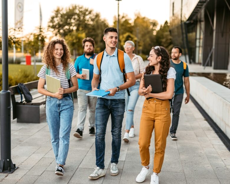 Group of friends walking on the university campus, holding books and notebooks.