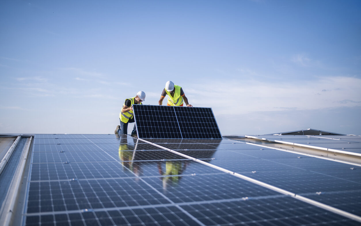 Team of two engineers installing solar panels on industrial factory roof.