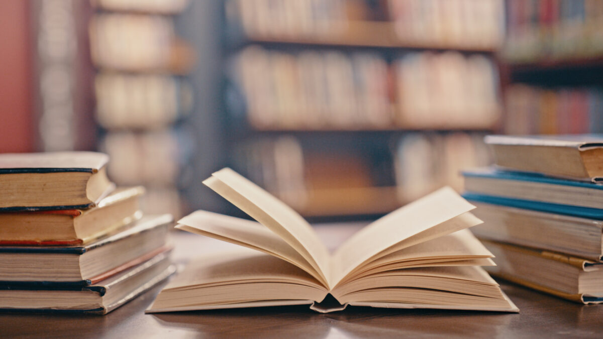 Library, books on table and background for studying, learning and research in education, school or college. Reading, philosophy and open, vintage or history print book, university blurred background