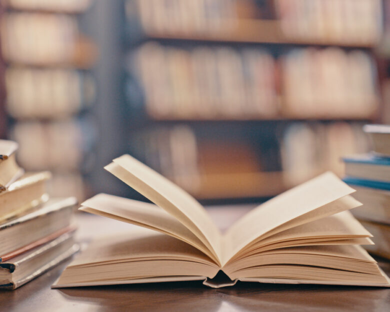 Library, books on table and background for studying, learning and research in education, school or college. Reading, philosophy and open, vintage or history print book, university blurred background