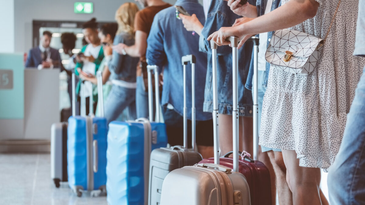Travelers with luggage using smart phones while waiting in line for boarding at airport. Focus on wheeled luggage.