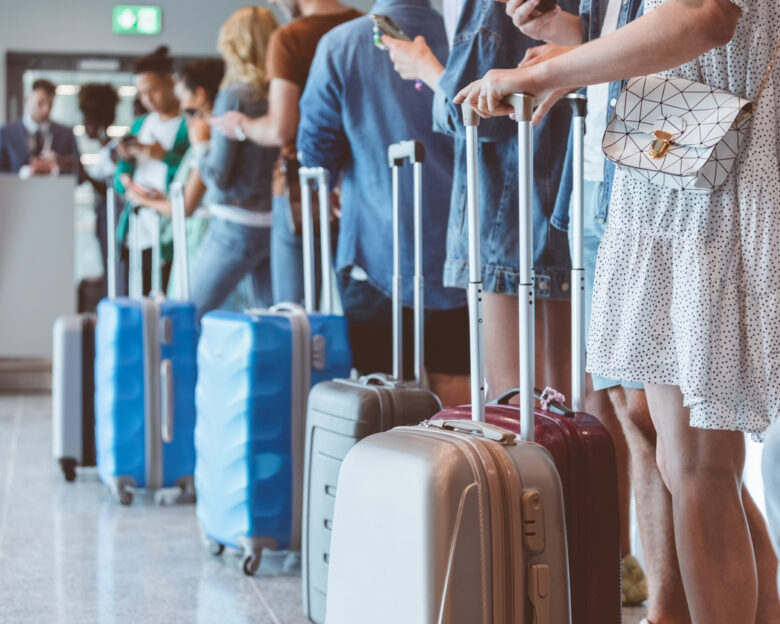 Travelers with luggage using smart phones while waiting in line for boarding at airport. Focus on wheeled luggage.