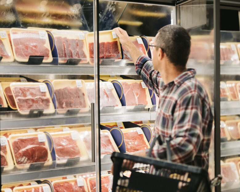 Male customer with a shopping basket taking meat from a fridge at local supermarket