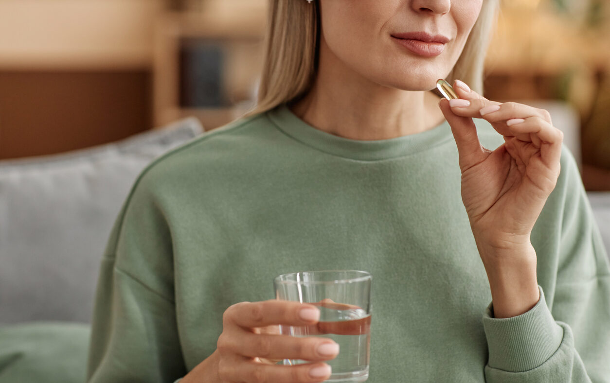 Minimal close up of adult woman taking vitamin pill and holding glass of water at home copy space