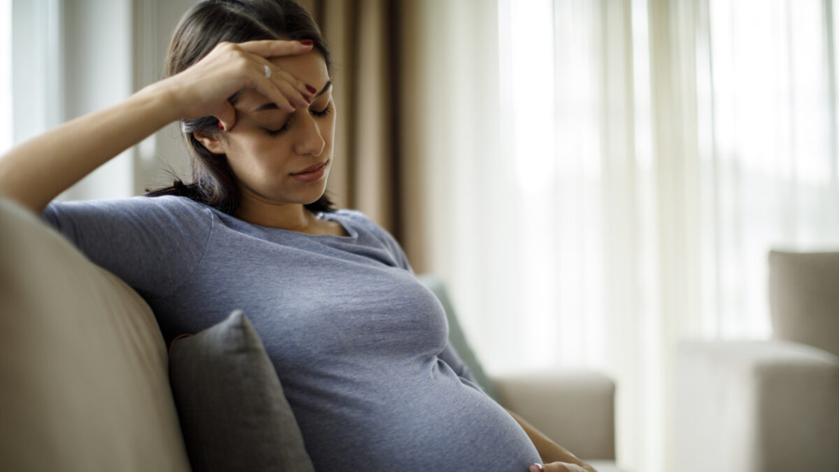 Tired stressed pregnant woman sitting on a couch and holding her belly