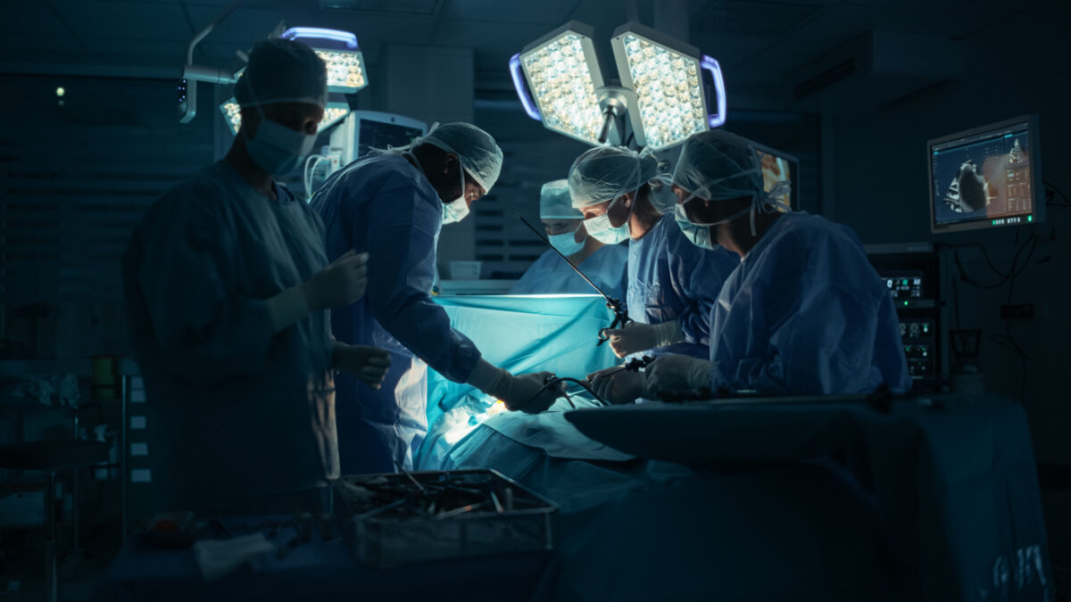 Diverse Surgical Team Working in a Darkened Operating Room Surrounded by Advanced Medical Equipment. Doctors Performing a Complex Surgery with the Help of Laparoscopic Equipment