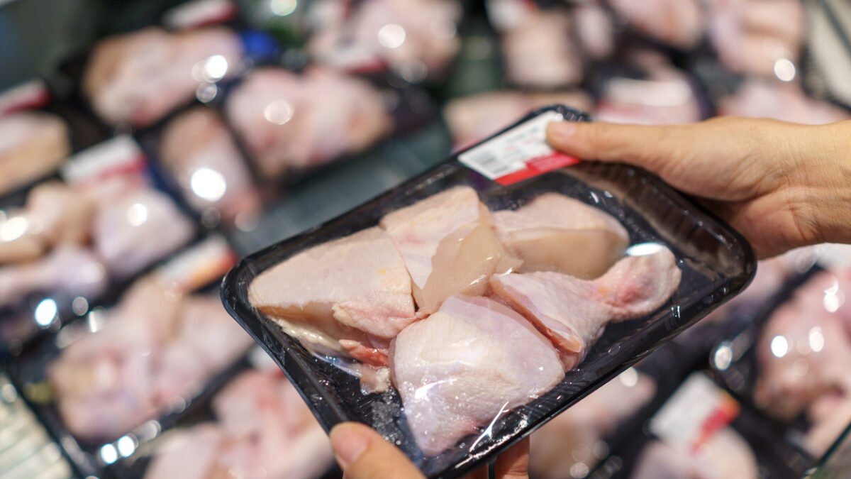 Shopper examining a tray of packaged raw chicken pieces in the supermarket meat section.