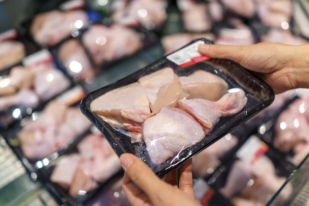 Shopper examining a tray of packaged raw chicken pieces in the supermarket meat section.