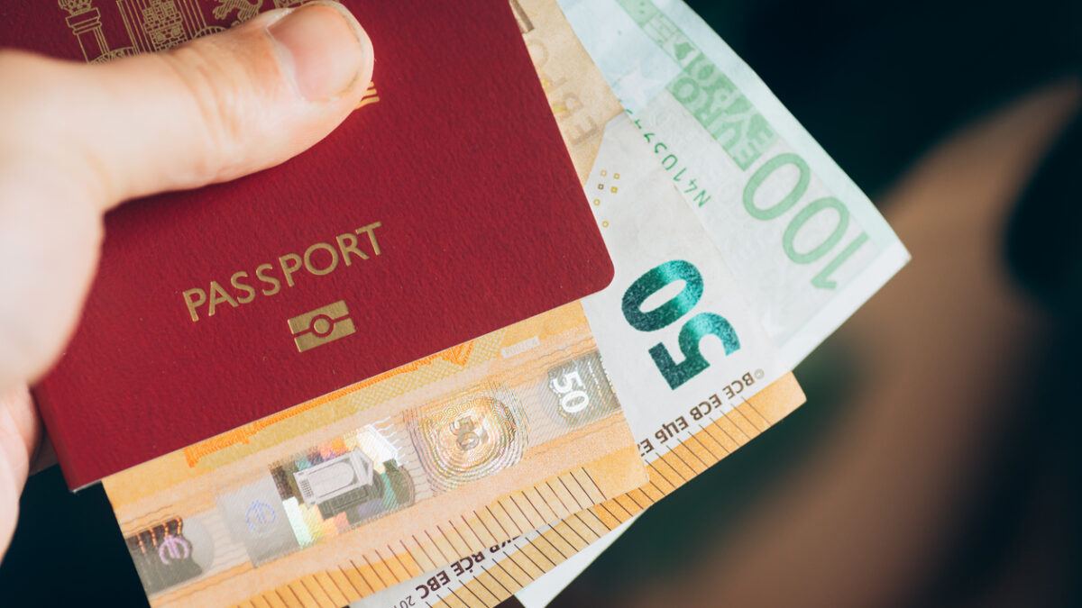 A hand holding a passport with money inside