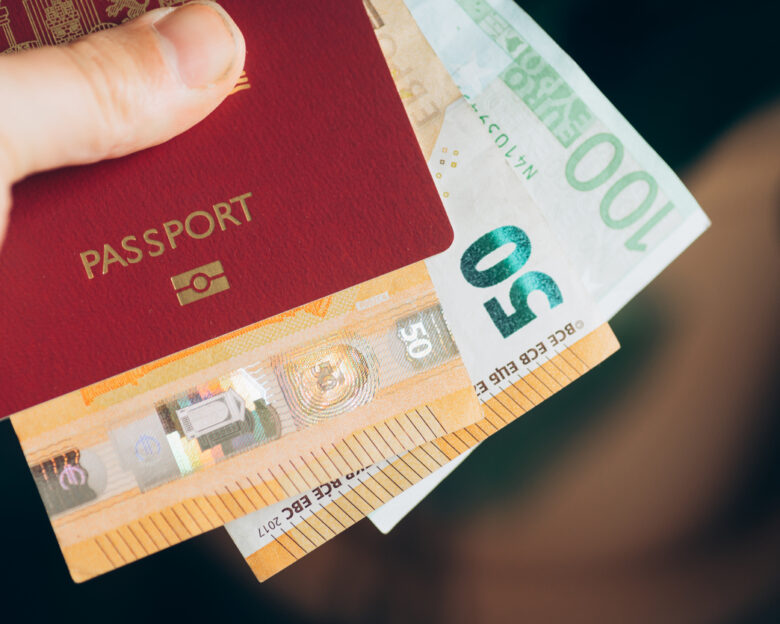 A hand holding a passport with money inside